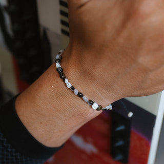 Hand wearing a dark mother of pearl bracelet over a patterned background