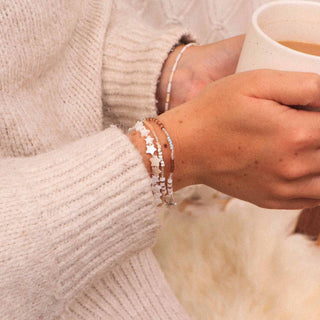 Person wearing two beaded bracelets holding a mug, with a soft focus background