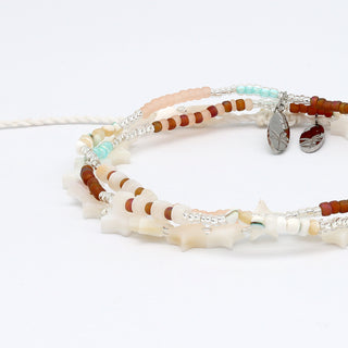 Close up of two beaded bracelets in neutral tones and star beads on a white background