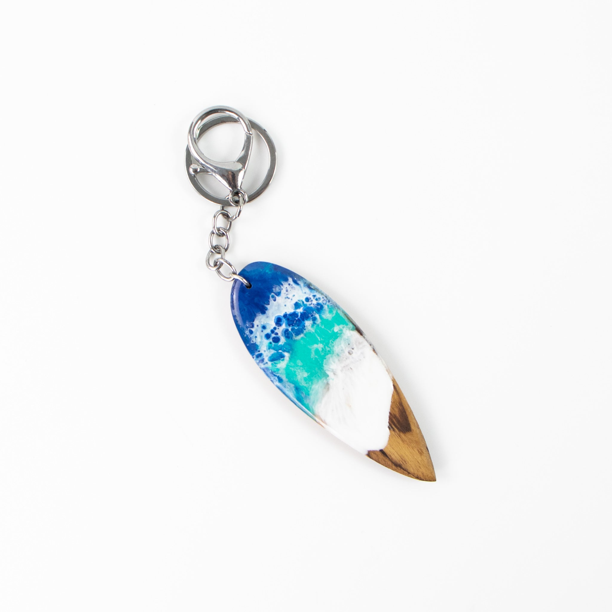 Wooden surfboard-shaped keyring with resin blue and white wave design, on a white background