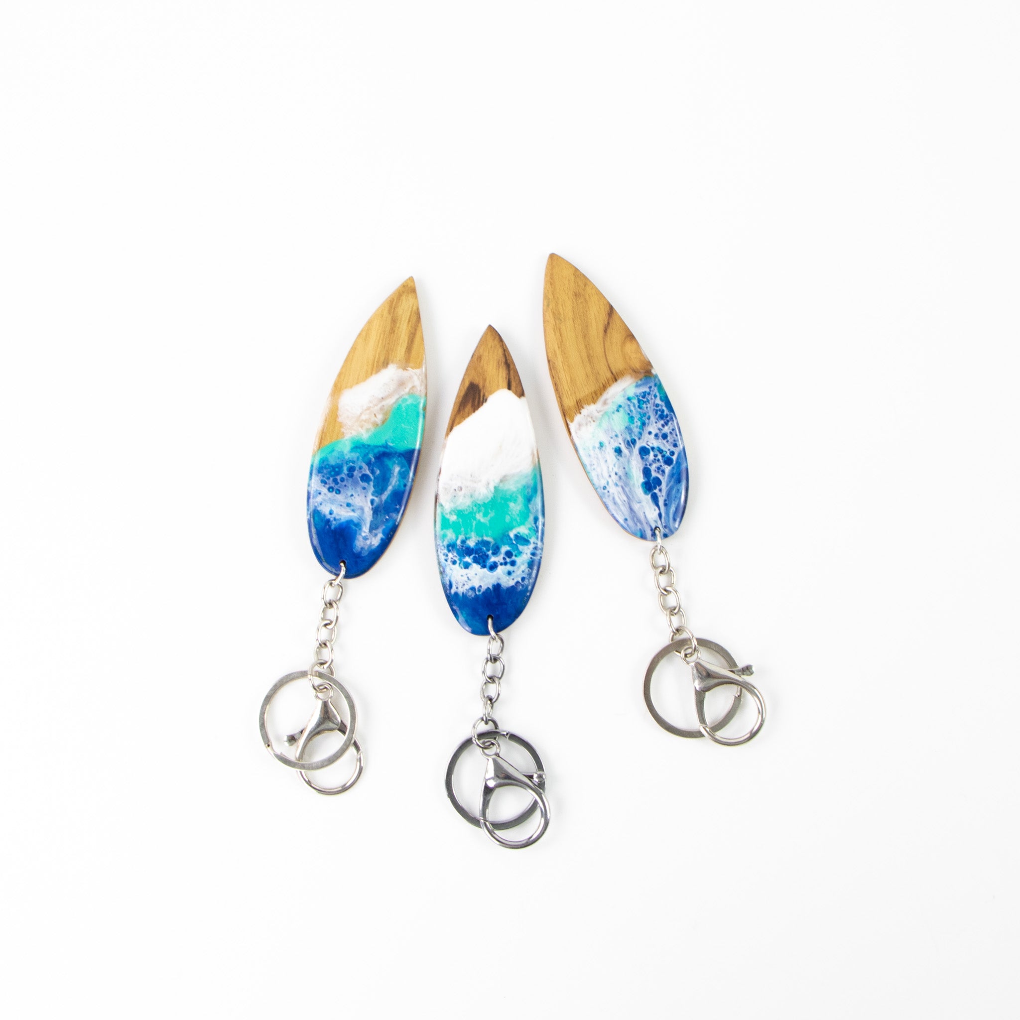 Three wooden surfboard shaped key rings with resin wave design, on a white back ground