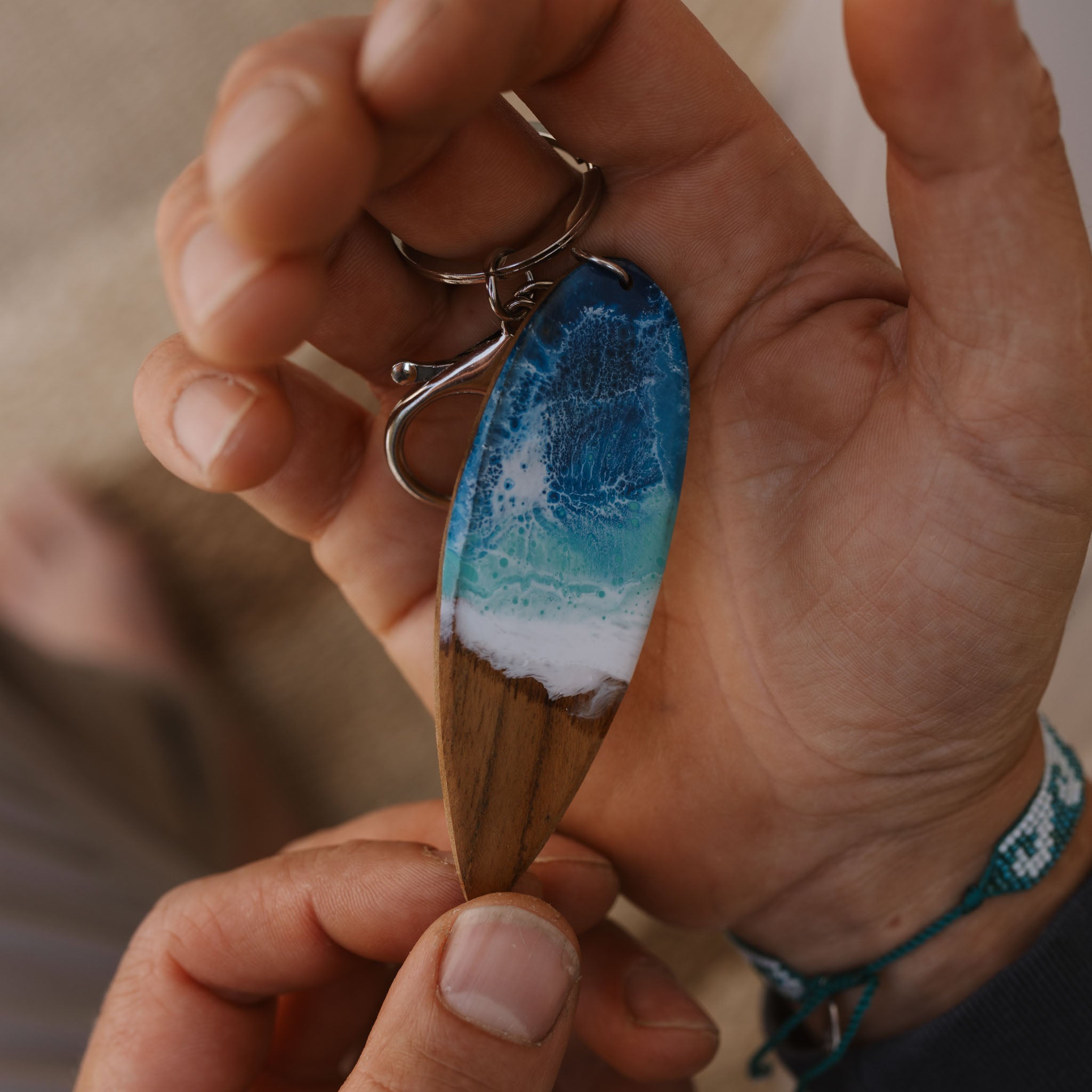 Hand holding our wood & resin surfboard keyring