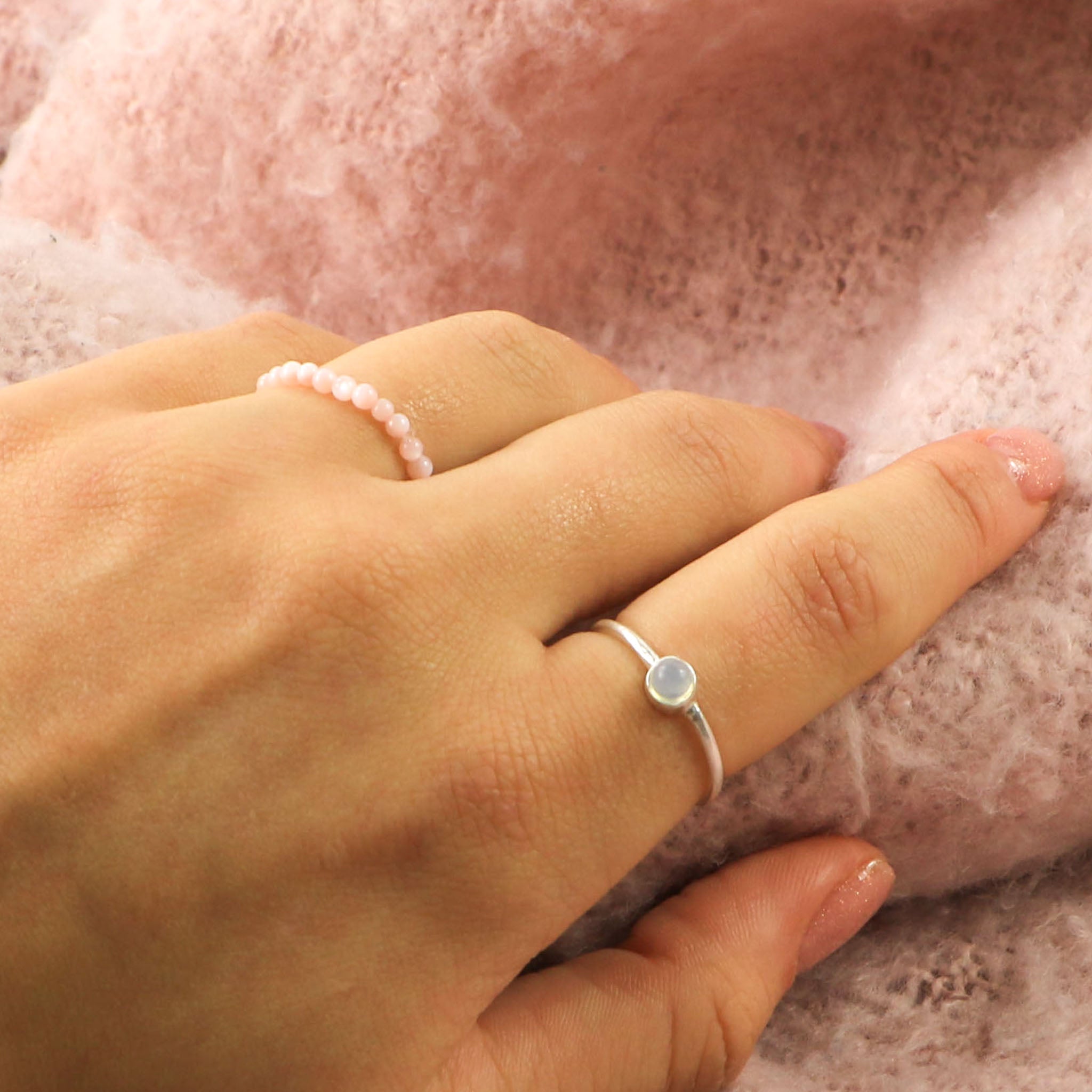 A hand wearing our white agate, silver-plated ring and a limited edition, pink mother-of-pearl beaded stretchy ring.