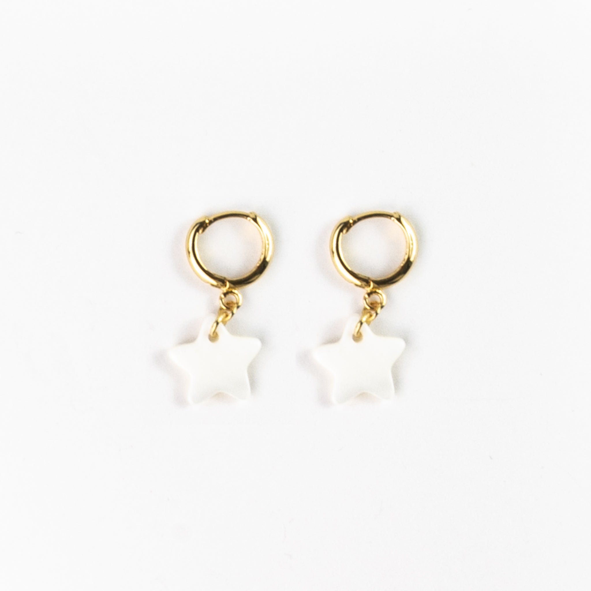 Celestial inspired star charm earrings, gold-plated copper alloy huggie hoop earrings with star shaped flat motehr-of-pearl charms. Pictured flat on a white background.