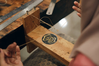 Person threading a needle with a wooden table and sewing supplies in the background