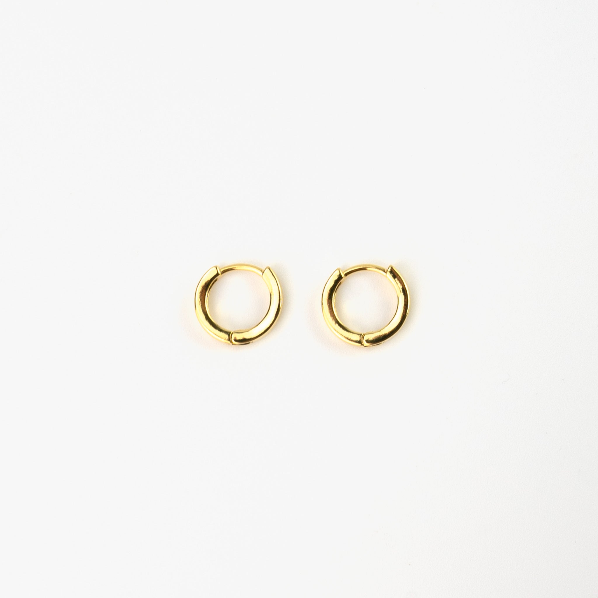 Minimalist gold-plated copper alloy huggie hoop earrings. Tiny huggie hoops great for stacking, pictured flat on a white background.