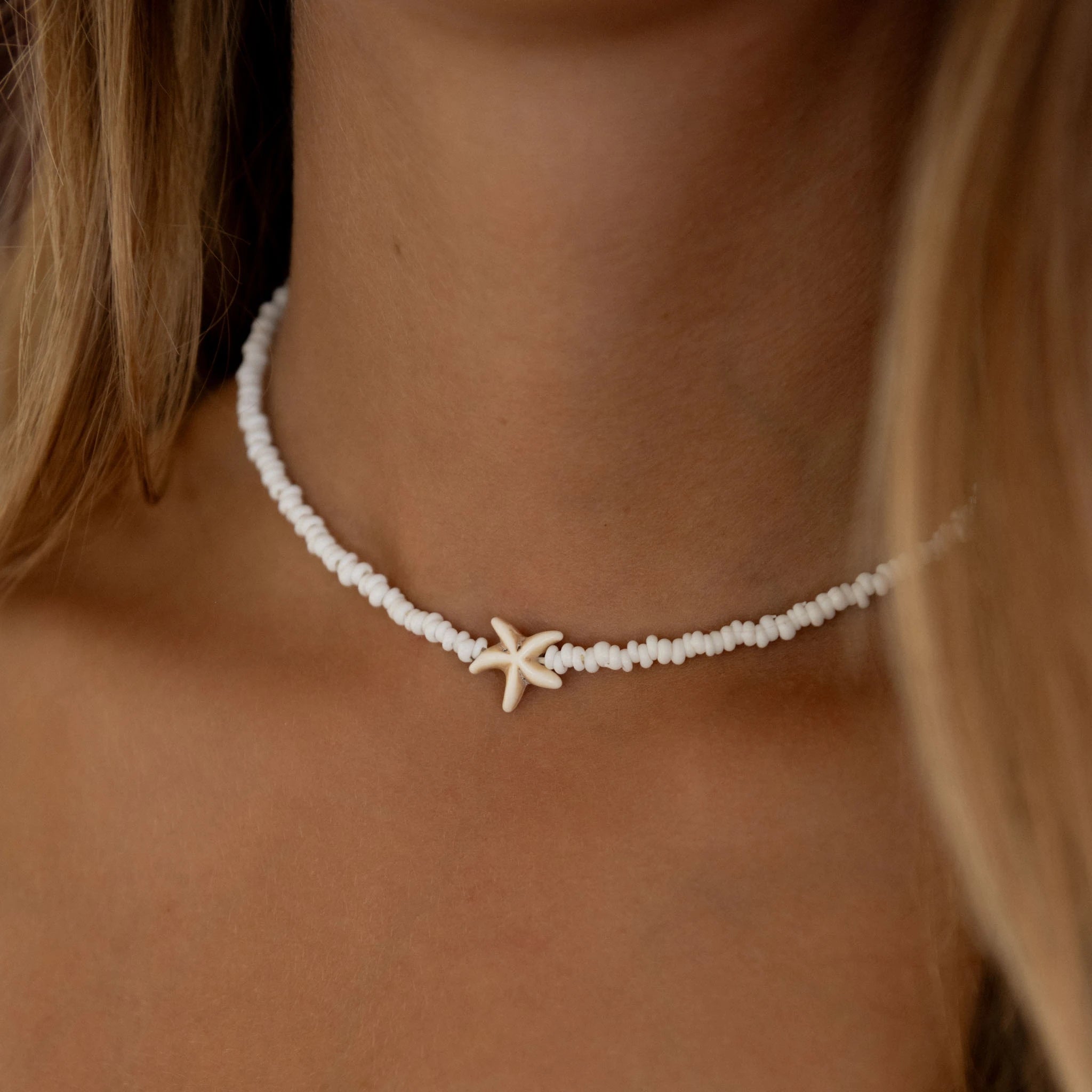 Our best selling, white frosted glass bead and starfish charm necklace on a models neck