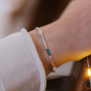 Close-up of a wrist wearing a dainty beaded bracelet with blue toned, white and turquoise beads
