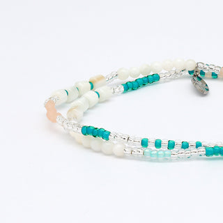 Close up of multi-strand beaded bracelet with turquoise, white, and beige beads on a white background