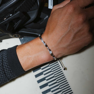 Close up of a persons wrist wearing dark beaded bracelet, resting on a surfboard