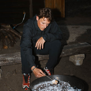 Person roasting marshmallows on an open fire in a dark setting, wearing beaded bracelets