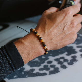 Hand wearing a gemstone beaded bracelet over the top of a snowboard