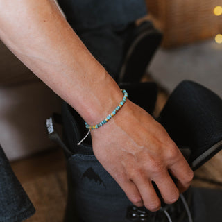 Hand wearing a turquoise stone bracelet holding a ski boot
