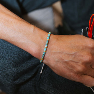 Close-up of a wrist wearing a turquoise beaded bracelet with a dark fabric background