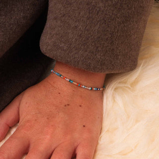 Close-up of a hand wearing a beaded bracelet on a soft beige blanket