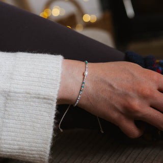 Close-up of a hand wearing a dainty beaded bracelet with blurred lights in the background