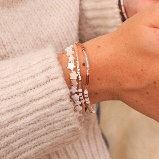 Close-up of a wrist wearing two bracelets, wearing a beige knitted jumper