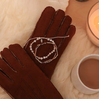 Two beaded bracelets in neutral tones and star beads on a pair of brown gloves, with a warm background