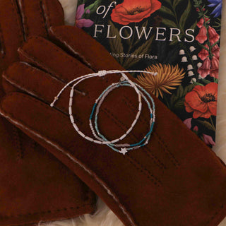 Two bracelets on a brown pair of gloves with a floral book in the background