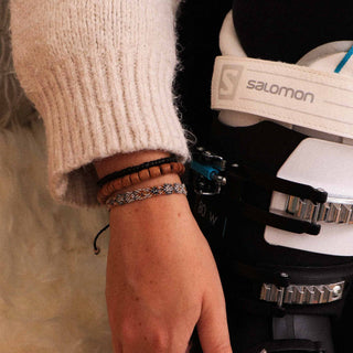 Close-up of a wrist and hand with three bracelets holding ski boots, with 'Salomon' branding visible.