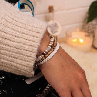 Close-up of a person's wrist with bracelets, wearing a beige sweater, in a cozy indoor setting.
