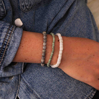 Close-up of a person wearing three beaded bracelets wearing a denim jacket