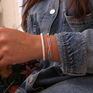 Person wearing two beaded bracelets on a wrist with a denim jacket