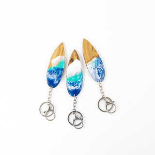 Three wooden surfboard shaped key rings with resin wave design, on a white back ground