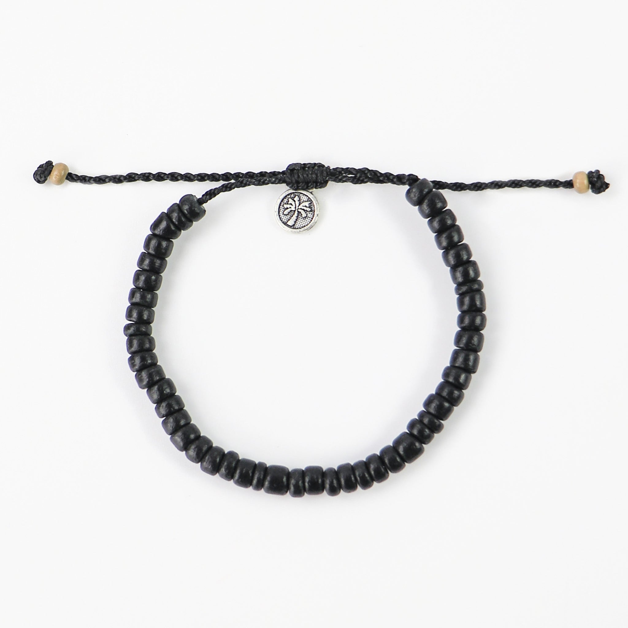 Black painted wood beaded bracelet. Coconut wood beads, painted black, are threaded onto a natural cream coloured wax polyester cord and finished with our signature textured palm tree tag.