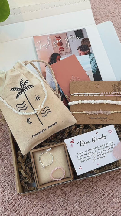 A models hands putting on our limited edition Galentines letterbox set, including a silver ring, a pink stretchy beaded ring, and three pink and white bracelets.